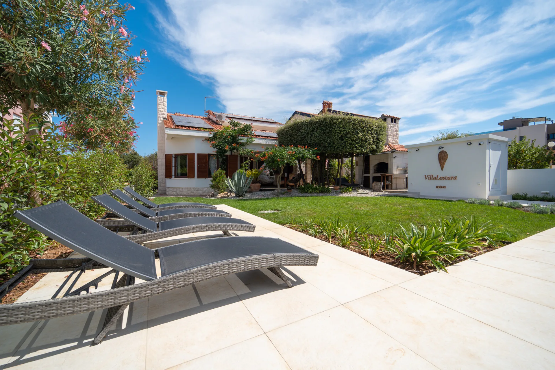 Villa Lostura’s garden, sun loungers and the villa name on the wall in Kožino